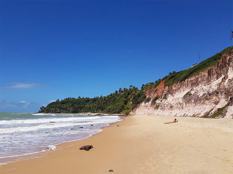 Praia do Giz com menina sozinha na areia e cercada por falésias