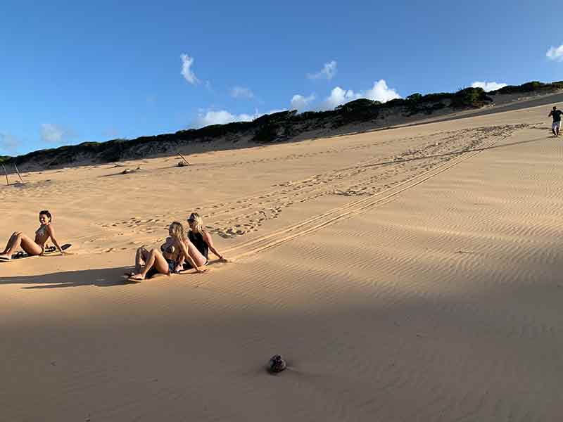 Pessoas descem a Duna de Cacimbinhas em dia de céu azul