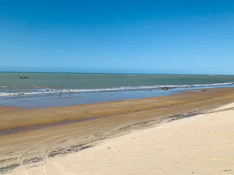 Mar calmo e praia de Monte Alegre vazia com duas pessoas caminhando