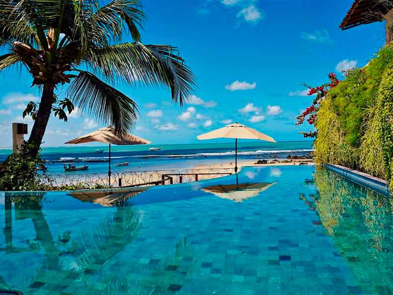 Piscina de borda infinita em dia de céu azul com guarda-sol na Pousada Marlin's, na Praia de Pipa