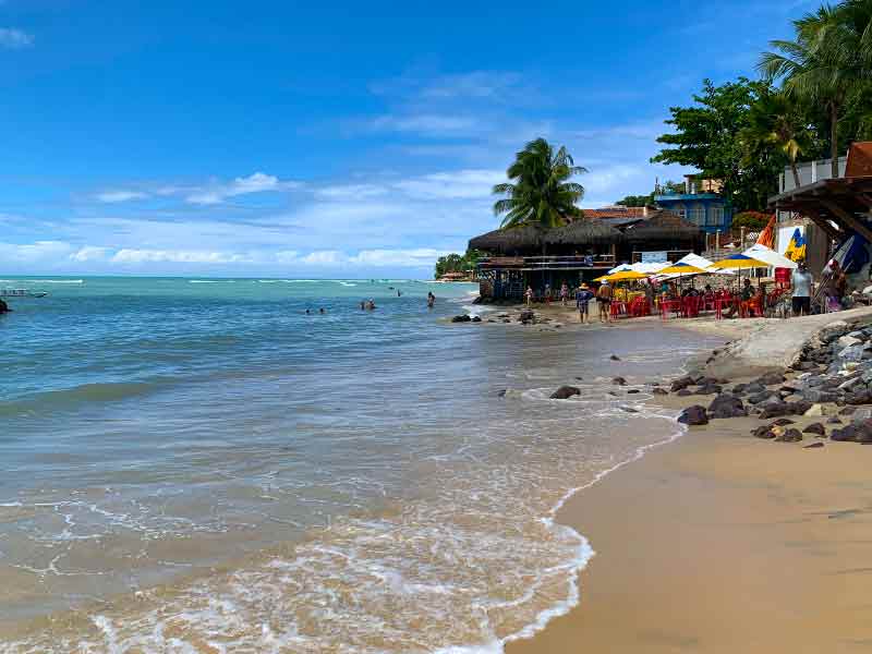 Mar em dia de céu azul com barraca à frente na Praia do Centro, na Praia de Pipa