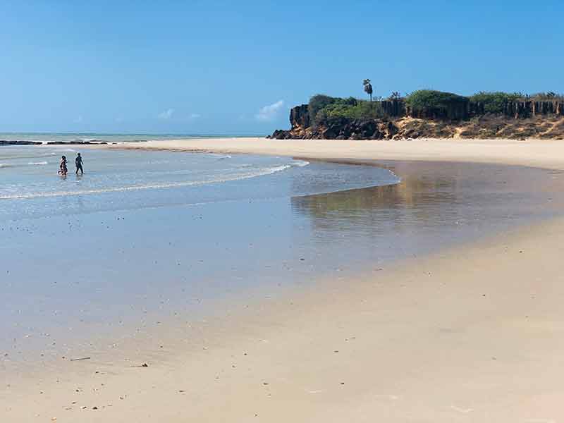 Duas pessoas se divertem no mar de Tourinhos com areia vazia em dia de céu azul