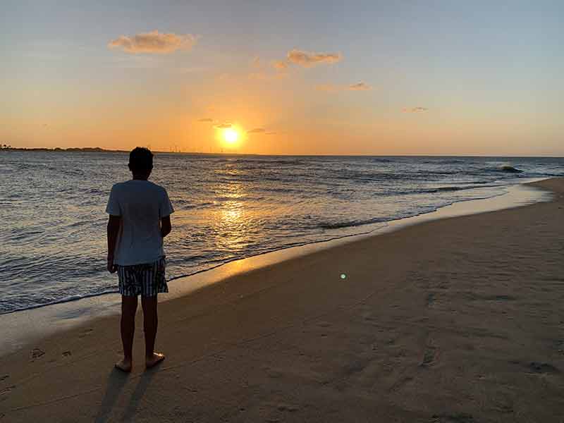 Homem na areia assiste ao pôr do sol no mar de Tourinhos, em São Miguel do Gostoso