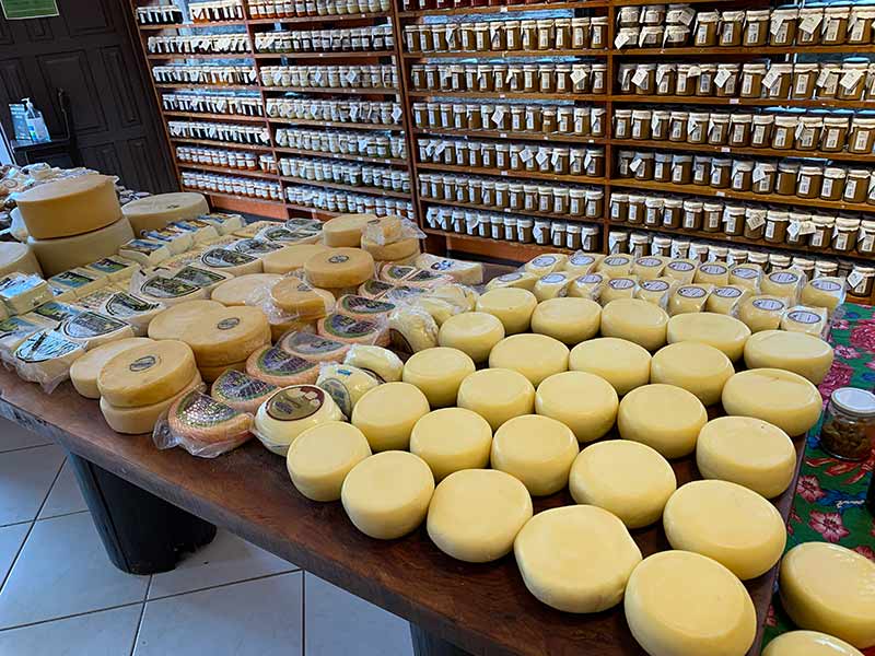 Mesa com diversos queijos e prateleiras com doces na loja A Pioneira em Gonçalves