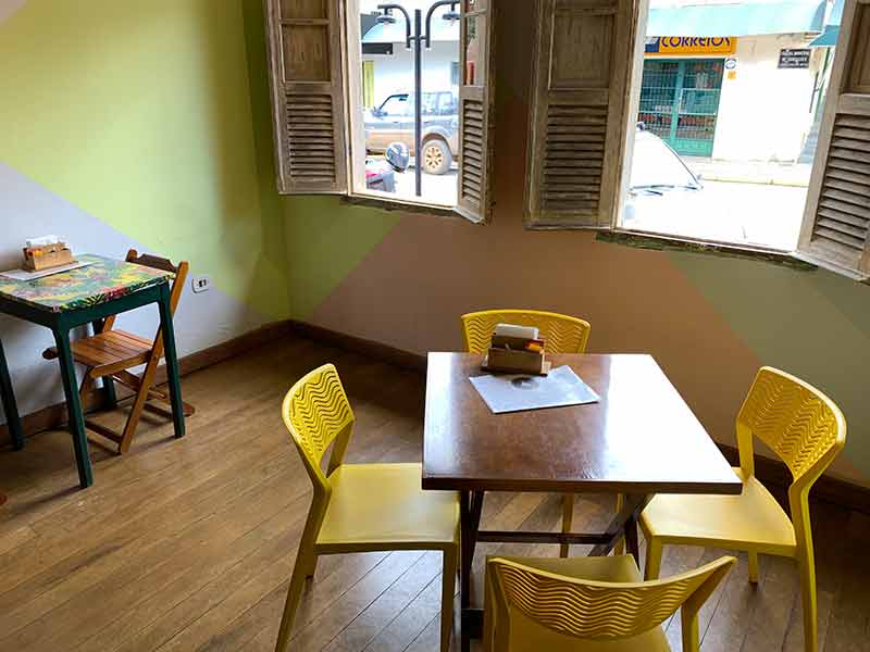 Área interna da Ararosa com mesas vazias e cadeiras amarelas