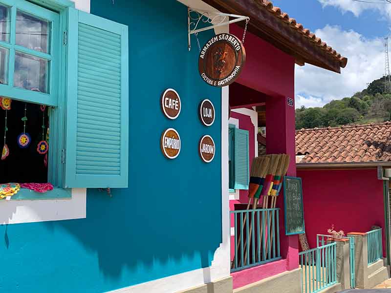 Entrada do Armazém São Bento, em Gonçalves, com parede azul e rosa e vassouras coloridas
