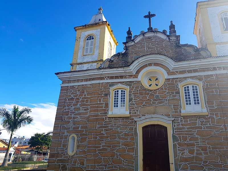 Igreja Matriz de Carrancas com céu azul e coqueiro ao fundo