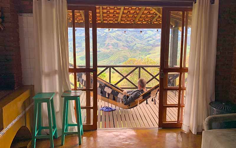 Homem deitado em rede observa a vista das montanhas na Pousada Morada do Luar