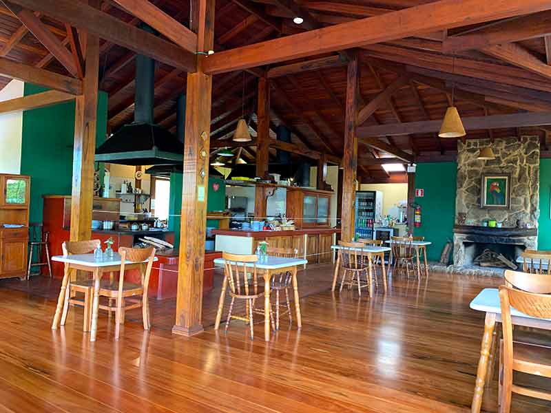 Área interna do restaurante Sauá, em Gonçalves, com piso de madeira e mesas e cadeiras vazias