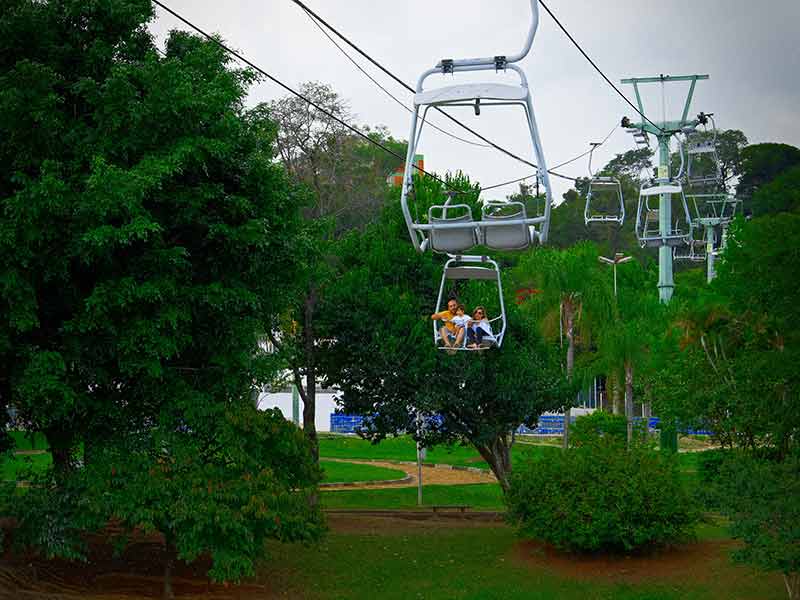 Pessoas andam de teleférico em Atibaia em meio às árvores