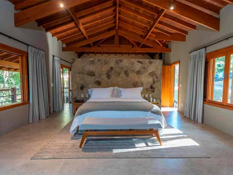 Quarto espaçoso do Canto do Irerê, dica entre os hotéis em Atibaia, com cama de casal e parede de pedras