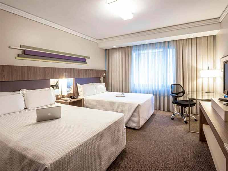 Quarto do Grand Mercure Rayon, em Curitiba, com duas camas de casal, carpete e cadeira