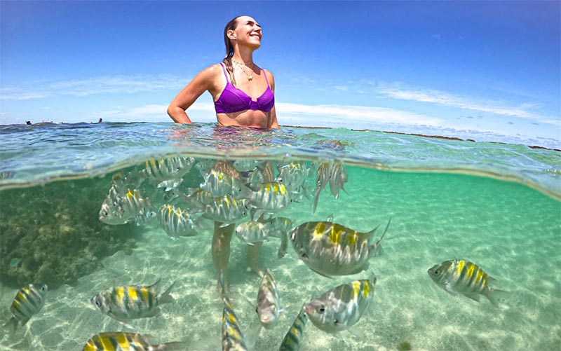 Mulher em pé com peixes nas Piscinas Naturais de Japaratinga