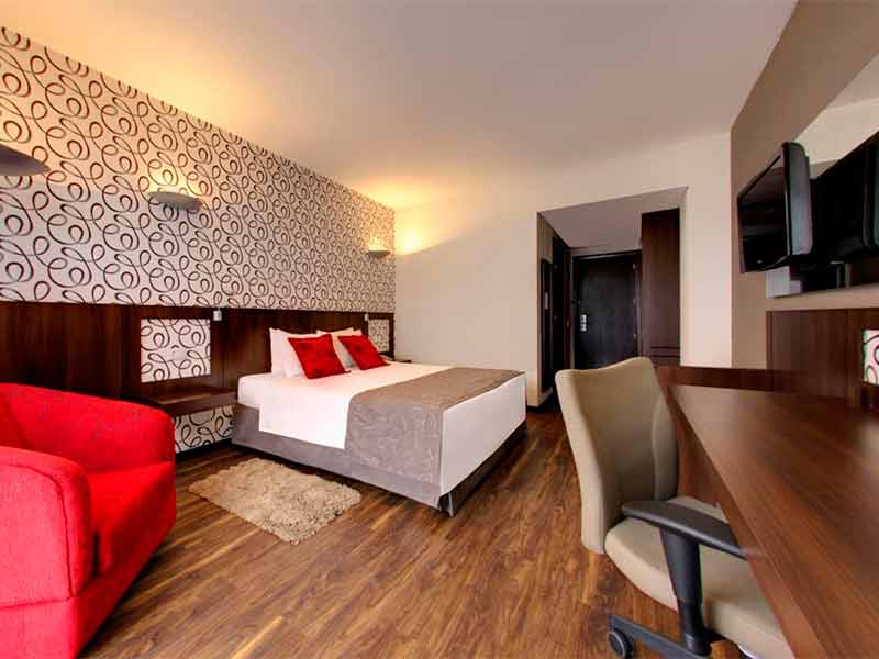 Quarto do Hotel Quality, dica de onde ficar em Curitiba, com cama de casal, poltrona vermelha e mesa de trabalho