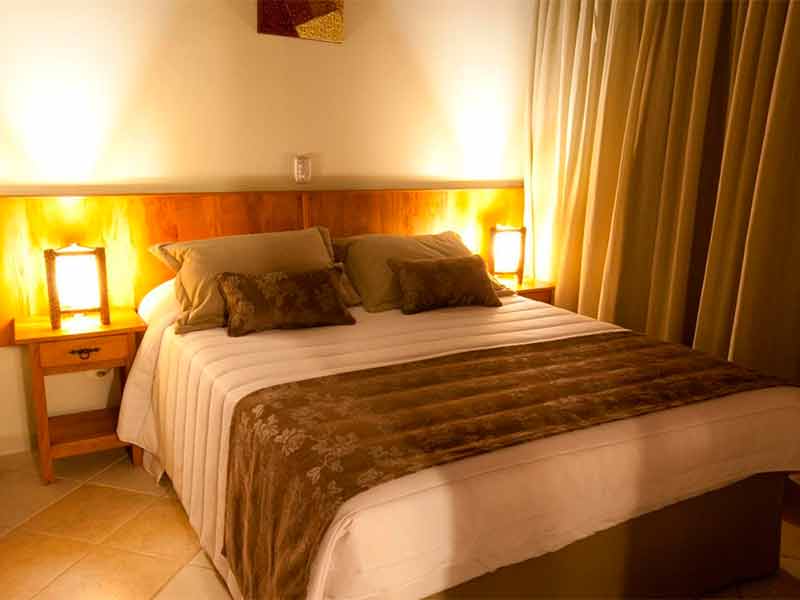 Quarto do Refúgio do Saci, um dos hotéis em Atibaia, com cama de casal, luminárias e cortina