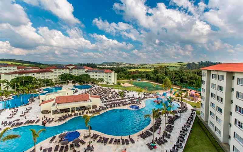 Vista das piscinas e dos prédios em dia de céu azul com nuvens no Tauá Resort