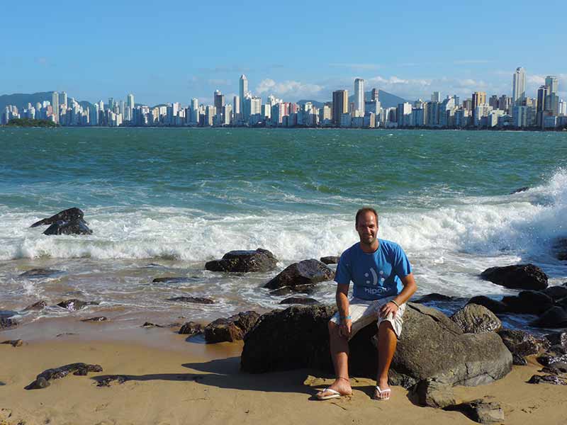 Homem posa sentado em pedra de frente para o mar na Praia do Canto, em Balneário Camboriú