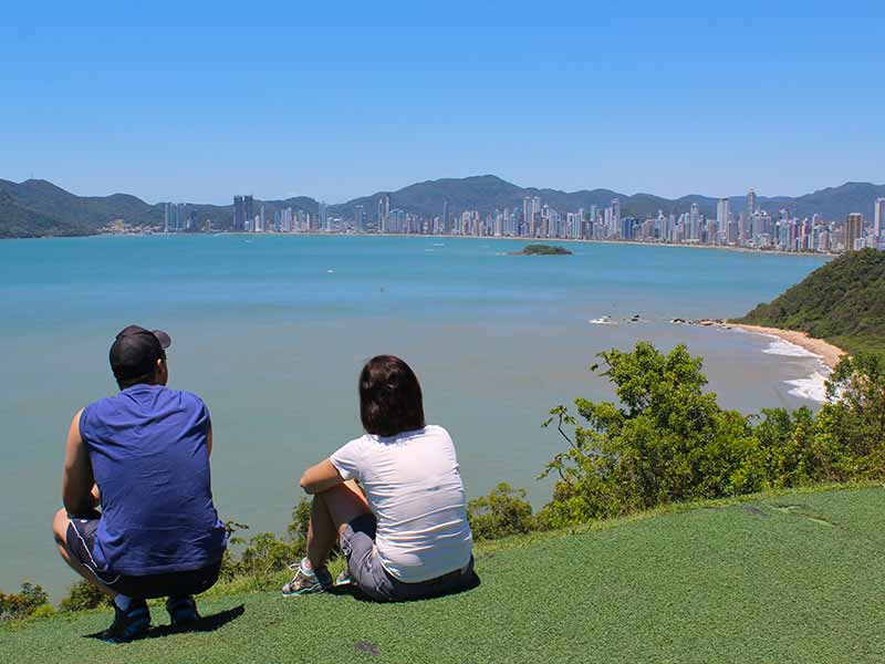 Homem e mulher observam a praia no Morro do Careca em dia de céu azul