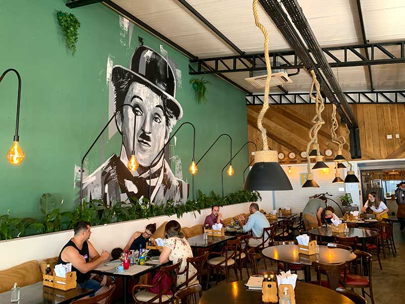 Ambiente do restaurante Chaplin com mesas ocupadas e desenho do artista na parede