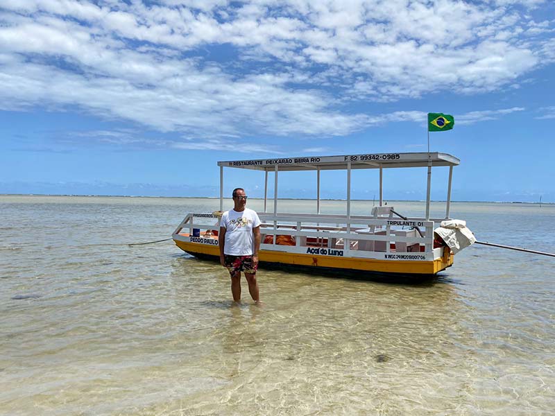 Homem em pé em frente a barco na Praia do Patacho