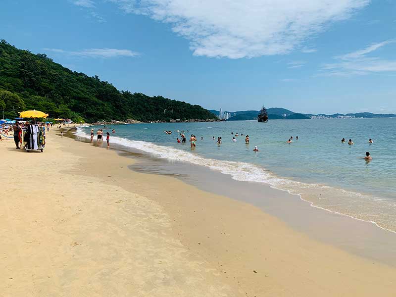 Pessoas nadam e outras na areia na praia de Laranjeiras, em Balneário Camboriú