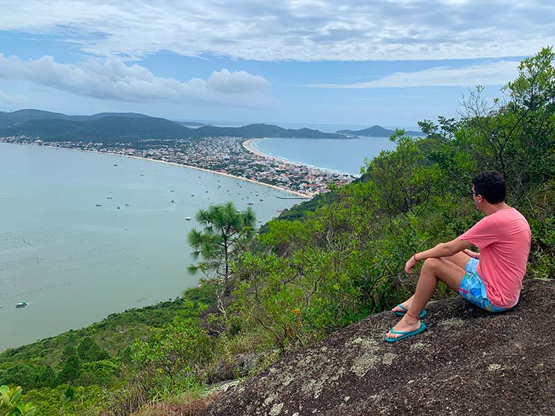 Homem sentado em pedra observa a vista no Mirante Eco 360º, em Bombinhas, Santa Catarina