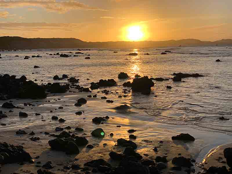 Pôr do sol no mar entre as pedras na Praia do Centro, em Pipa