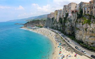 Vista da praia de Tropea, na Itália, com casas sobre paredão de rochas