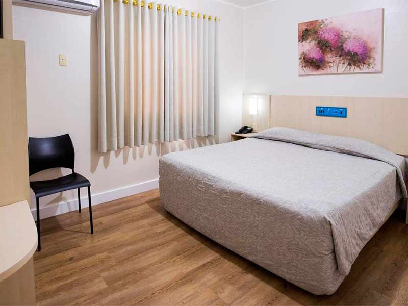 Quarto do Bella Camboriú com cama de casal, cadeira vazia e quadro na parede