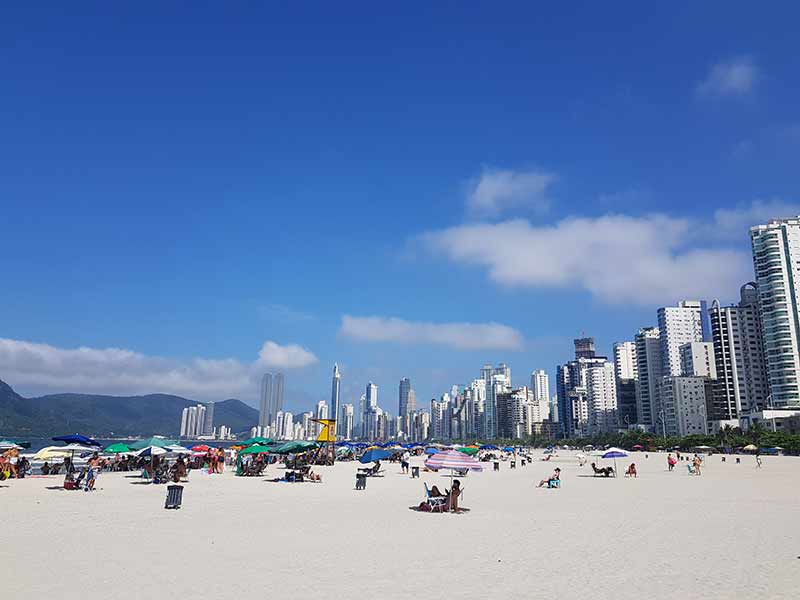 Prédios ao fundo e pessoas na areia aproveitando o dia de sol na Praia Central, em Balneário Camboriú