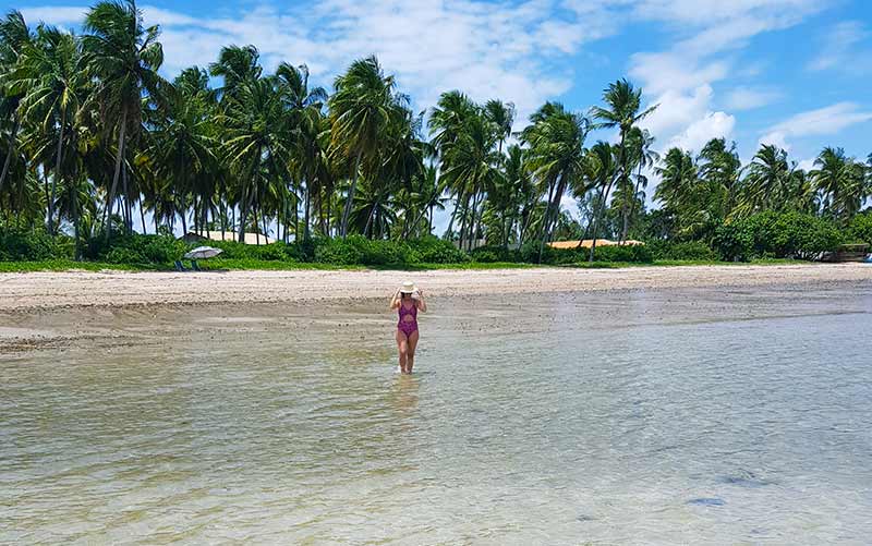 Mulher caminha nas águas calmas da Praia do Patacho em Alagoas