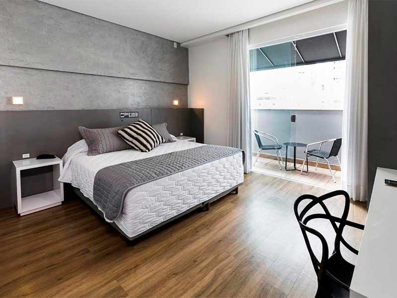 Quarto espaçoso do Tropykalia Gold Hotel, dica de onde ficar em Balneário Camboriú, com cama de casal e piso de madeira