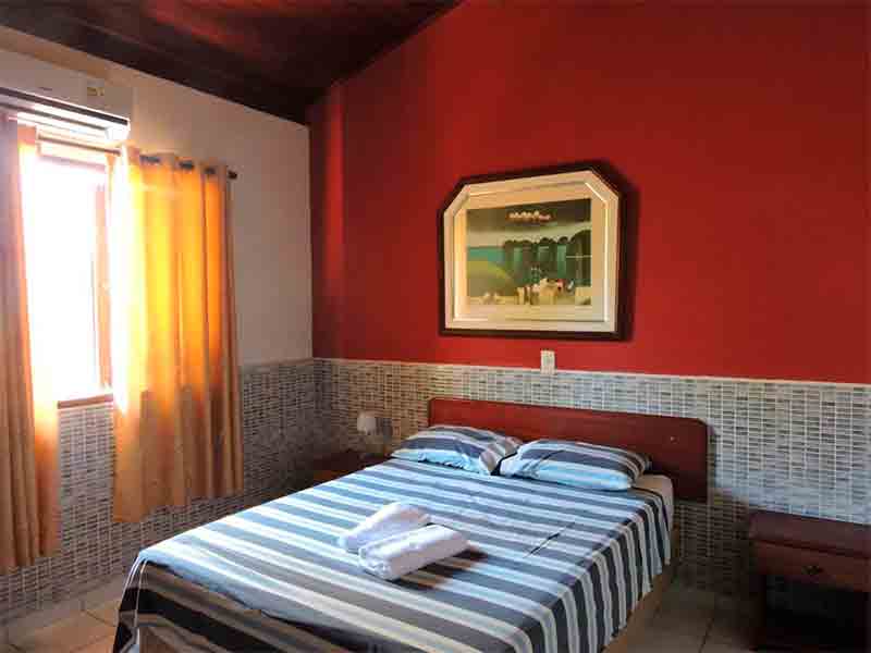 Quarto da Village Miramar, dica de onde ficar na Praia de Antunes, com parede vermelha e cama de casal