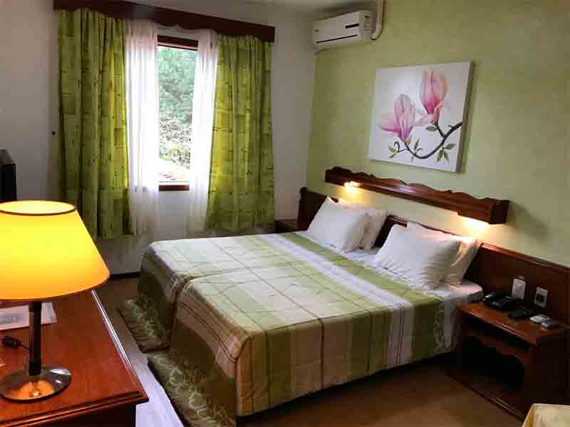 Quarto do Bergblick com duas camas juntadas, cortinas verdes e abajur
