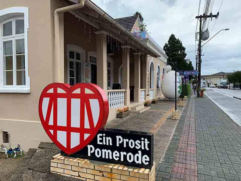 Placa na entrada da loja Ein Prosit em dia de céu nublado