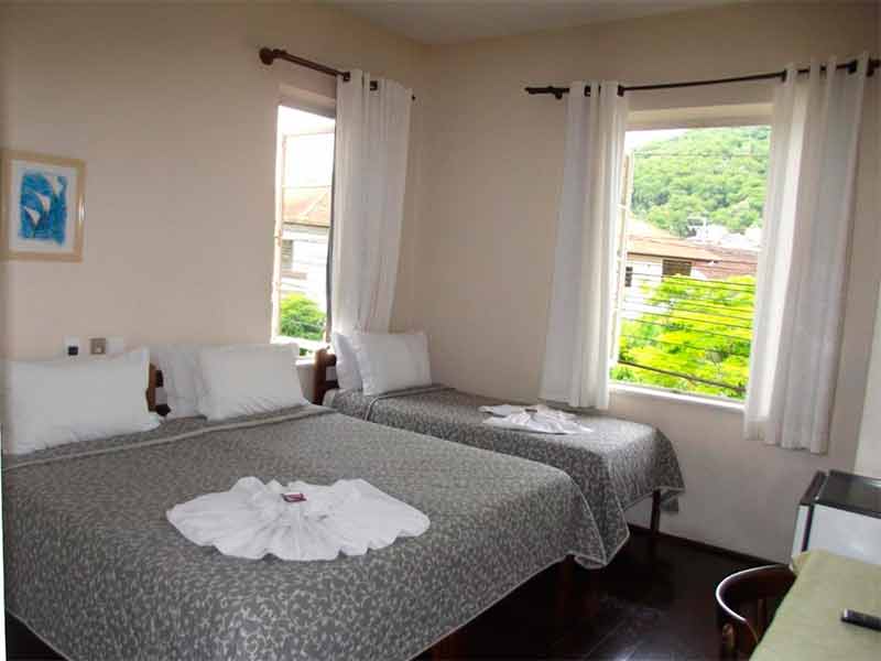 Quarto da Pousada Max, dica entre as pousadas em Pomerode, com cama de casal e cama de solteiro e chão de madeira