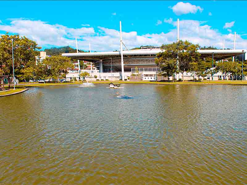 Lago com construção na frente em dia de céu azul com poucas nuvens do Parque Ramiro Ruediger (Foto: Site oficial do parque)