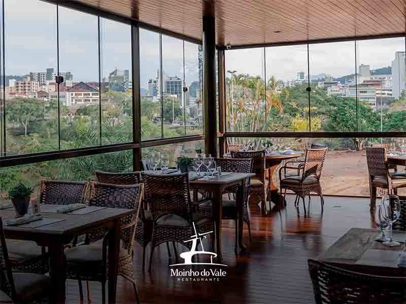 Varanda do restaurante Moinho do Vale com mesas e janelas de vidro (Foto: Instagram do restaurante)