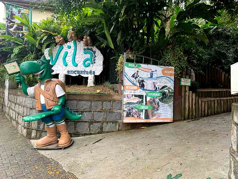 Dinossauro na entrada da Vila Encantada, dica de o que fazer em Pomerode, com banner sobre atrações do parque