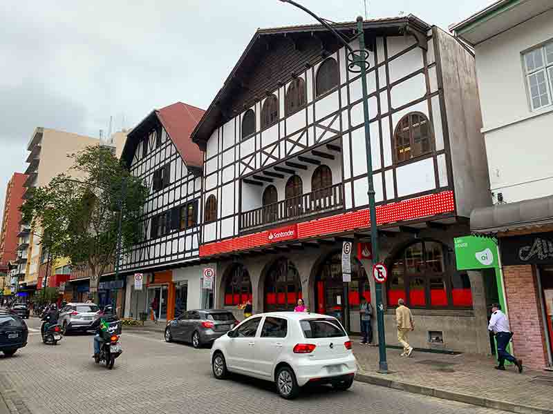 Carros passam em frente a um banco com construção no estilo enxaimel na XV de Novembro, dica do que fazer em Blumenau