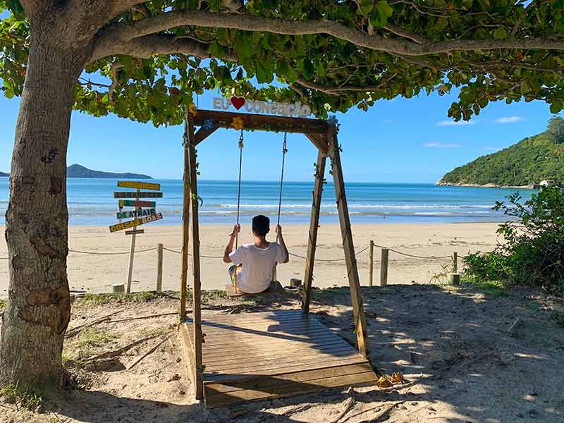 Homem sentado em balanço olhando para a Praia da Conceição