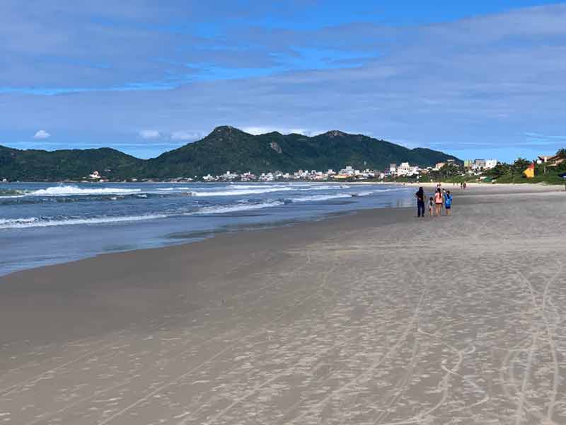Pessoas caminhando na areia e mar com ondas na praia de Mariscal