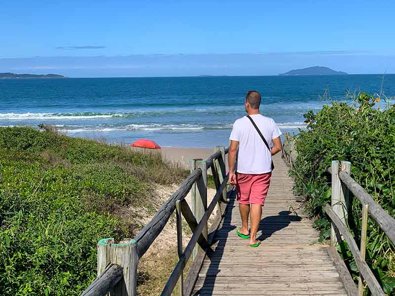 Homem caminha por passarela indo para a praia de Quatro Ilhas