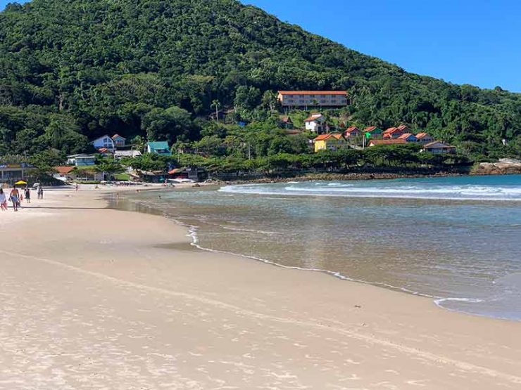 Pessoas caminham na areia enquanto o mar está vazio na praia de Quatro Ilhas, em Bombinhas, SC