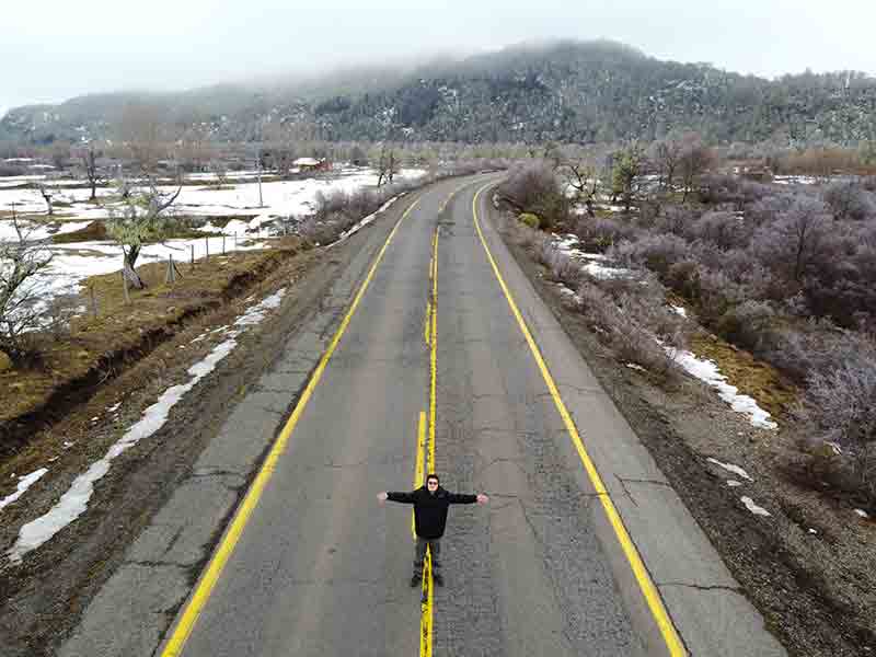 Homem de braços abertos no meio da estrada com neve ao lado na Araucanía, no Chile