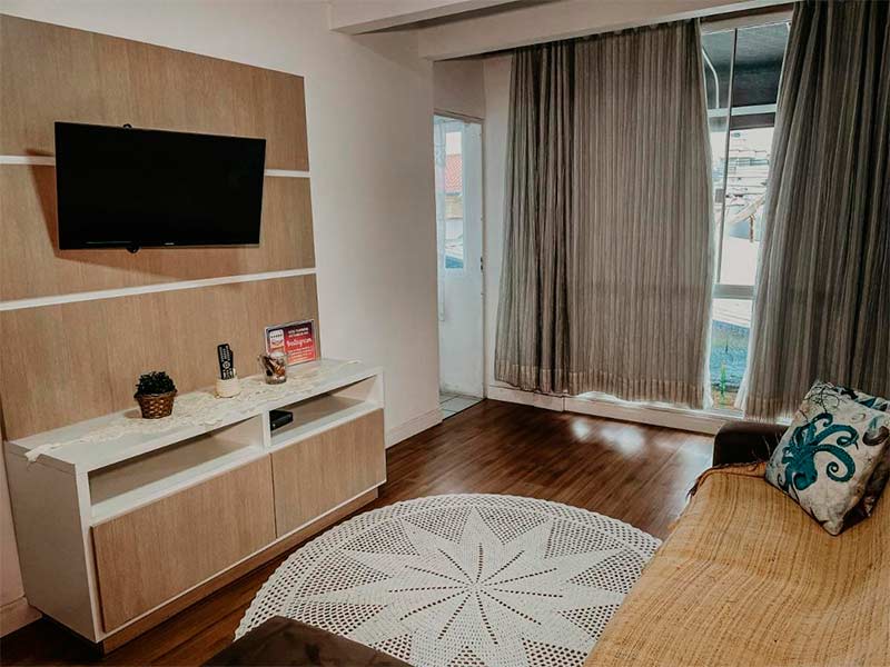 Sala de estar de acomodação da Canto do Pescador, dica entre as pousadas em Bombinhas, com TV, tapete e sofá