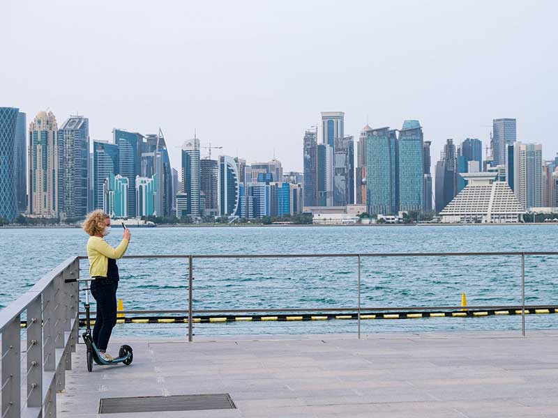Mulher utiliza celular em frente aos prédios de Doha, no Qatar