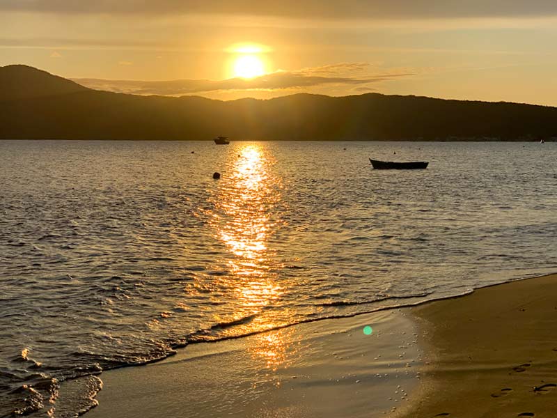 Pôr do sol nas montanhas com mar à frente e barquinho na praia de Canto Grande, em Bombinhas