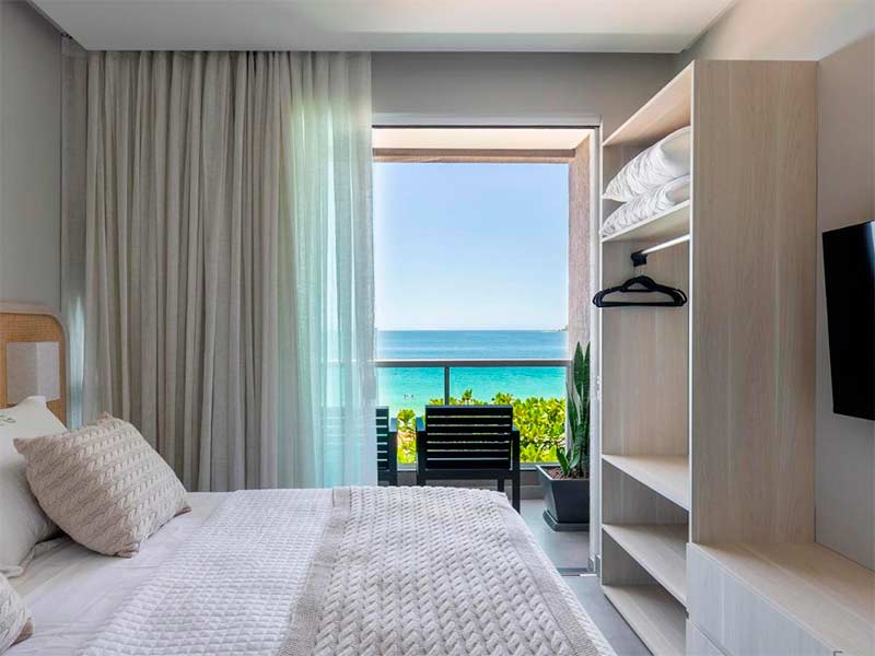 Quarto da Pousada Gaúcha com cama de casal, guarda-roupa e varanda com vista para o mar de Bombinhas