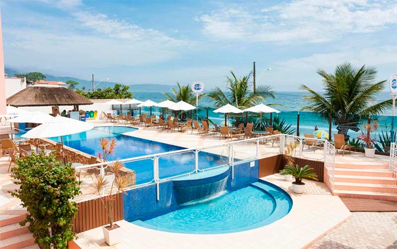 Área externa com piscina e espreguiçadeiras da Vila do Coral, dica entre as pousadas em Bombinhas, em dia de céu azul com poucas nuvens